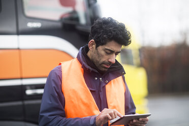 Mann mit reflektierender Weste benutzt Tablet bei Lastwagen - SGF02185