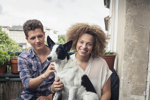 Porträt einer lächelnden Frau mit Hund, die mit einem Freund auf einem Balkon sitzt, lizenzfreies Stockfoto