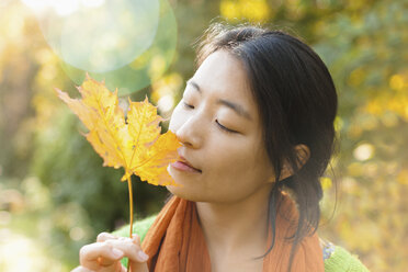 Nahaufnahme einer jungen Frau mit geschlossenen Augen, die ein trockenes Ahornblatt in einem Park an einem sonnigen Tag hält - FSIF01040