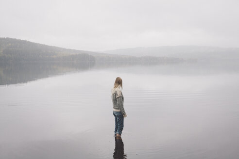 Woman standing in lake against sky during foggy weather, Jaervsoe, Haelsingland, Sweden - FSIF01058