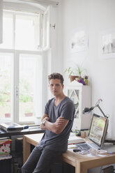 Portrait of handsome man leaning with arms crossed on table at home - FSIF01071