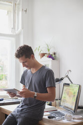 Junger männlicher Universitätsstudent, der zu Hause ein digitales Tablet benutzt - FSIF01076