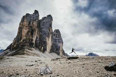 Low angle view of teenage boy jumping over rocks in alps against cloudy sky, South Tyrol, Italy stock photo