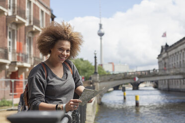 Porträt einer lächelnden Touristin, die mit einer Landkarte vor dem Fernsehturm steht, Berlin, Deutschland - FSIF01091