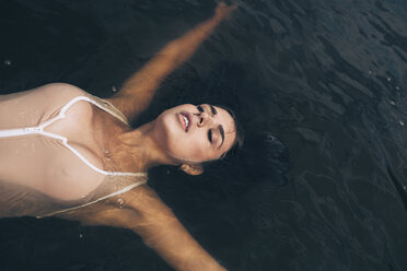 High angle view of sensuous young woman with arms raised floating on lake - FSIF01111