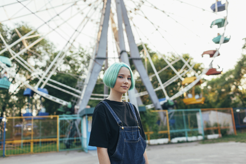 Portrait of smiling teenage girl standing against Ferris wheel at park stock photo