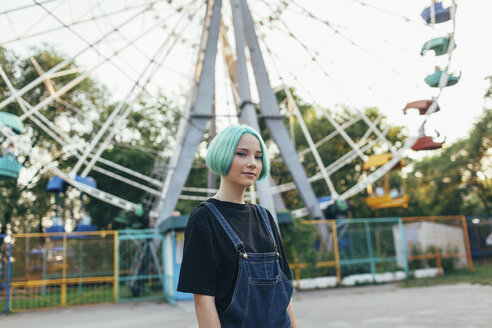 Portrait of smiling teenage girl standing against Ferris wheel at park - FSIF01114