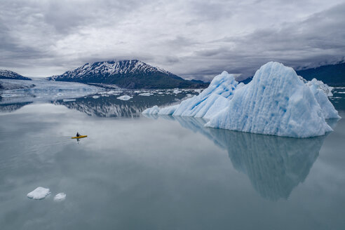 Person beim Kanufahren in einer Lagune mit Eisbergen vor bewölktem Himmel, Lake George, Palmer, Alaska, USA - FSIF01128
