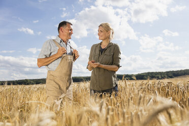 Happy mature couple talking while standing amidst crops at farm against sky - FSIF01148