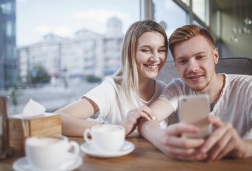 Glückliches junges Paar, das ein Mobiltelefon benutzt, während es im Restaurant sitzt - FSIF01170