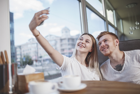 Glückliches junges Paar, das ein Selfie mit dem Mobiltelefon macht, während es im Restaurant sitzt, lizenzfreies Stockfoto