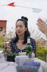 Nachdenkliche junge Frau, die ein Weinglas hält, während sie bei einer Party an einem Tisch im Freien sitzt - FSIF01176