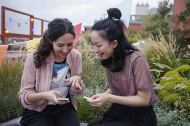 Glückliche Freundinnen benutzen Smartphones, während sie auf der Terrasse sitzen - FSIF01179