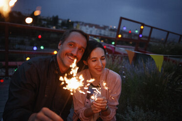 Happy couple holding sparklers on patio at night - FSIF01183