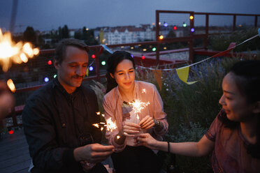 Male and female friends holding sparklers on patio - FSIF01187