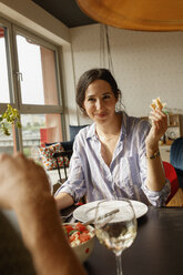 Lächelnde Frau mit Brot in der Hand und Blick auf einen Mann im Haus - FSIF01190