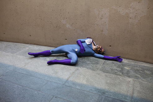 High angle view of unconscious superhero lying on footpath against wall - FSIF01195