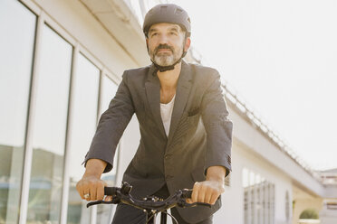 Niedriger Blickwinkel eines Geschäftsmannes, der an einem sonnigen Tag mit dem Fahrrad an einem Gebäude vorbeifährt - FSIF01200