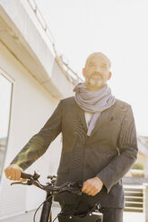 Low angle view of businessman with bicycle in city on sunny day - FSIF01201