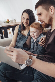 Lächelnde Eltern mit Tochter, die auf dem Sofa zu Hause auf ihren Laptop schaut - FSIF01210