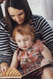 Mutter liest ihrer Tochter ein Buch vor, während sie zu Hause auf dem Sofa sitzt - FSIF01215