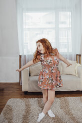 Happy girl with arms outstretched dancing on carpet at home - FSIF01218