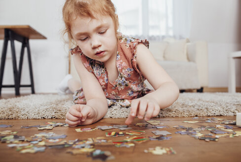 Mädchen spielt mit Puzzleteilen, während sie zu Hause auf dem Teppich liegt - FSIF01225