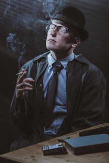 Young man sitting at table with gun while smoking cigarette - FSIF01231