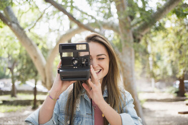 Happy young woman using instant camera at park - FSIF01240