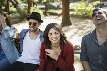 Cheerful male and female friends sitting on bench at park - FSIF01241