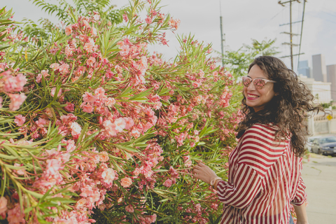 Glückliche erwachsene Frau neben rosa Blumen an einem sonnigen Tag, Los Angeles, Kalifornien, USA, lizenzfreies Stockfoto