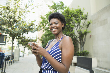 Side view of smiling young woman using mobile phone in city - FSIF01253