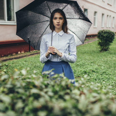 Porträt eines Teenagers, der einen Regenschirm hält, während er bei Regen auf einer Wiese steht, lizenzfreies Stockfoto