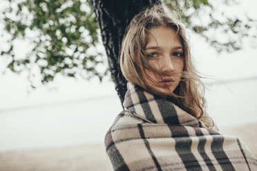 Portrait of teenage girl wrapped in blanket against lake on windy day - FSIF01261