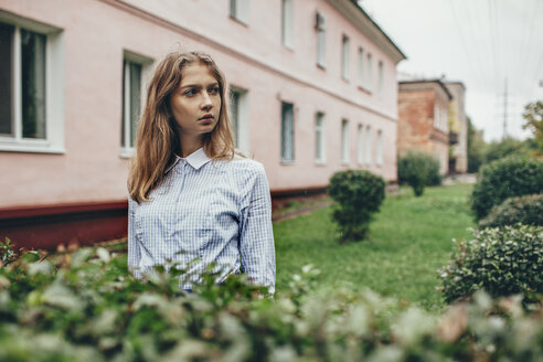 Nachdenkliches Teenager-Mädchen, das bei Pflanzen vor einem Gebäude steht - FSIF01262
