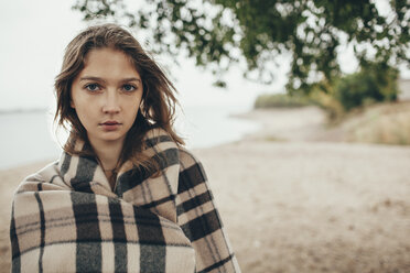 Portrait of teenage girl wrapped in blanket by lakeshore - FSIF01264