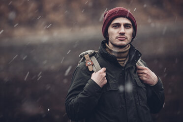 Porträt eines Mannes, der einen Rucksack trägt, während er im Freien bei Schneefall steht - FSIF01271