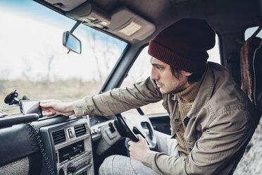 Man wearing knit hat and adjusting smart phone on dashboard of sports utility vehicle - FSIF01272