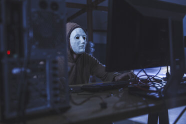 Mann mit Maske und Kapuze an einem Computer am Tisch - FSIF01282