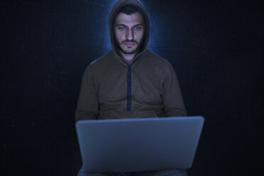 Junger Computer-Hacker in Kapuzen-Shirt mit Laptop vor schwarzem Hintergrund - FSIF01285