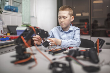 Serious boy operating machinery at table in classroom - FSIF01286