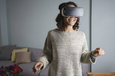 Happy woman using virtual reality headset while standing in living room - FSIF01327