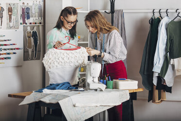 Auszubildender begutachtet den Stoff des Kleides eines Designers, der einen Kleiderbügel hält, im Modeatelier - FSIF01348