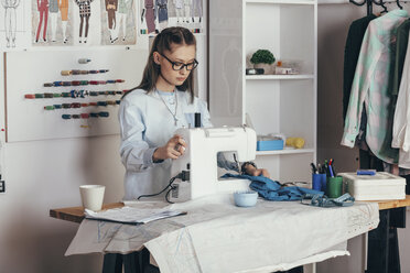 Female fashion designer using sewing machine at design studio - FSIF01349
