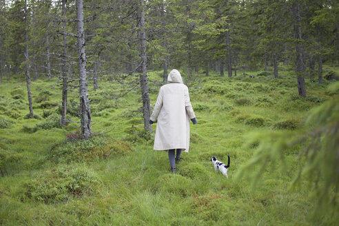 Rear view of woman wearing long coat while walking with cat on grassy field - FSIF01354