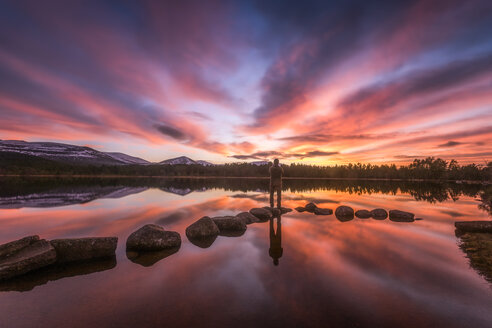 Vereinigtes Königreich, Schottland, Highlands, Cairngorms National Park, Loch Morlich, Sonnenuntergang, Wanderer steht auf Stein - SMAF00944