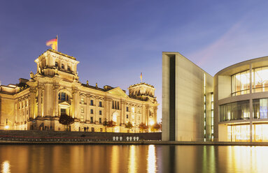 Germany, Berlin, Regierungsviertel, Reichstag building with German flags and Paul-Loebe-Building at Spree river in the evening - GWF05443