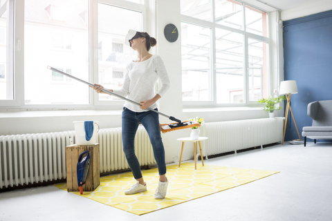 Vitale Frau zu Hause mit VR-Brille, die den Boden wischt, lizenzfreies Stockfoto