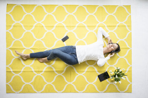 Lächelnde Frau mit Kopfhörern auf dem Teppich liegend mit einem Strauß Tulpen - MOEF00808