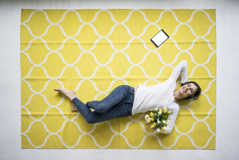 Lächelnde Frau mit Kopfhörern auf dem Teppich liegend mit einem Strauß Tulpen - MOEF00809